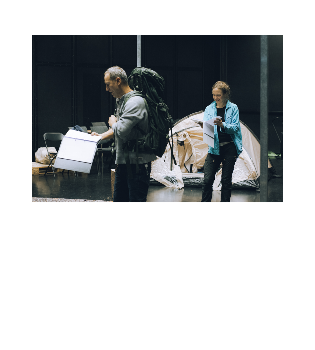 Skuespillere Jørn-Bjørn Fuller-Gee (med ryggsekk) og Gina Lindås Theodorsen leser fra manus foran et telt i et sort scenerom. Klikk på bildet for å lese om og se bilder fra leseprøven.